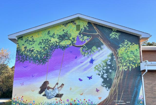 Vibrant mural showcasing a child on a swing, embraced by a flourishing tree, painted by artists Jake Seibert and Ibe Ananaba on a south-facing brick wall.