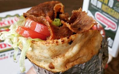 A close-up of a donair with donair meat, lettuce and tomato wrapped in tin foil. 
