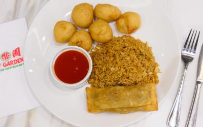 Chicken balls, fried rice and an egg roll served on a plate next to a May Garden-branded napkin.