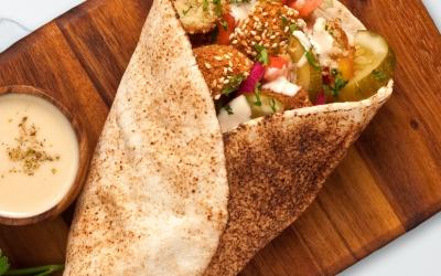 A falafel wrap served on a wooden cutting board.