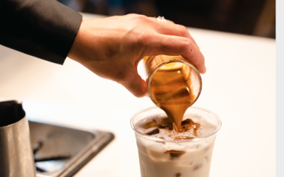 A barista pours espresso into an iced drink on a countertop.