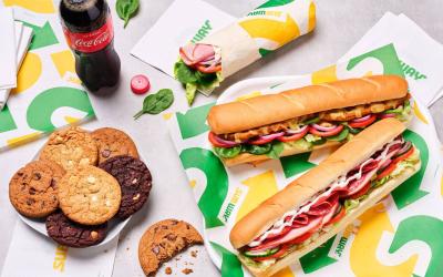 A flatly of two subs, cookies and a bottle of pop served on Subway-branded tissue.