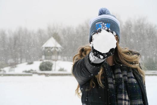 Woman holding a snowball in front of her face, wearing a Sackville Snow Days toque.